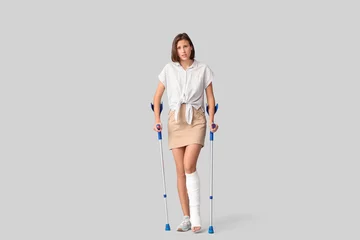 Selbstklebende Fototapeten Young woman with broken leg and crutches on light background © Pixel-Shot