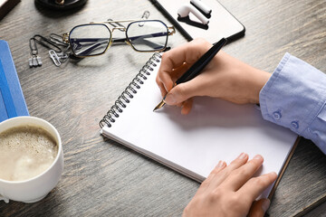 Obraz premium Female hands with blank notebook, fountain pen, cup of coffee, eyeglasses and mobile phone on wooden table, closeup