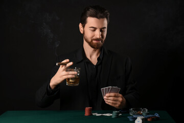 Handsome young man with whiskey and cigar playing poker at table in casino