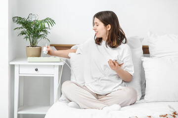 Young woman getting out mobile phone charger from extension cord in bedroom. National Day of...