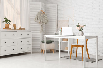 Stylish workspace with modern laptop and beautiful flowers in light home office