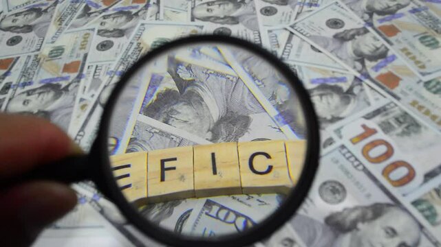 The word "DEFICIT" seen with a magnifying glass on a scattering of dollar bills. Economic and business concepts
