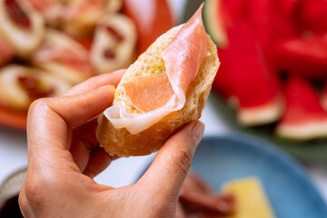 Woman holding a slice of bread with prosciutto and cheese