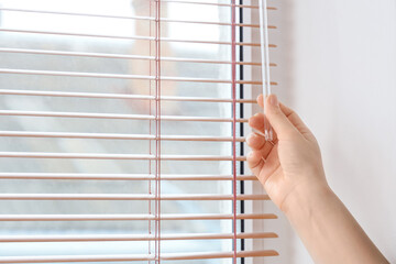 Female hand opening blinds on window in room, closeup