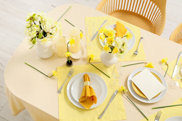 Elegant table setting with beautiful narcissus flowers, blank greeting card and folded napkins on plates