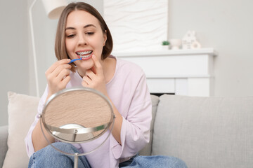 Young woman with dental braces and mirror cleaning teeth at home