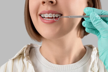 Doctor's hand checking woman's teeth with dental braces on light background, closeup