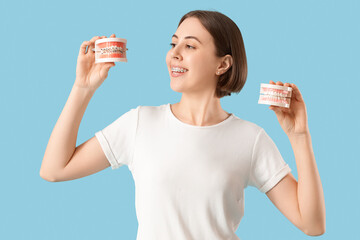 Young woman with dental braces and jaw models on blue background