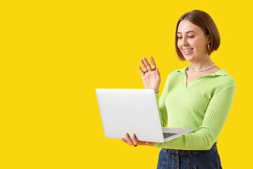 Young woman with dental braces and laptop video chatting on yellow background