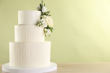 Delicious wedding cake decorated with flowers on wooden table against light green background, closeup. Space for text