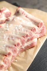 Raw pork ribs with sea salt on grey table, closeup