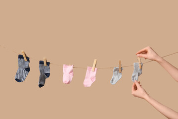 Hands with baby socks hanging on clothesline against beige background