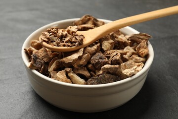 Pieces of dry chicory roots in bowl and spoon on dark table, closeup