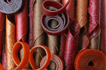 Delicious fruit leather rolls as background, top view