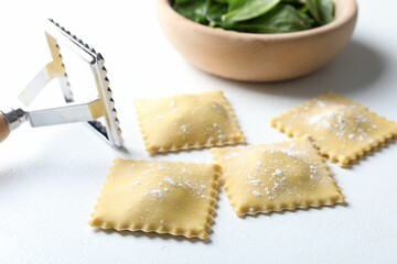 Uncooked ravioli, cutter and spinach on white table, closeup