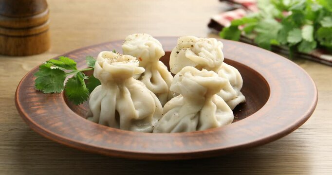 Woman adding cilantro to khinkali at wooden table, closeup