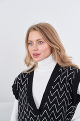 Young woman with loose blonde hair wearing a white turtleneck under a black sweater with a zigzag...