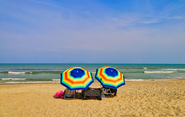 An ocean landscape on a sandy beach with two colorful umbrellas in the middle and green ocean waves under a blue sky. Carolina Beach, Wilmington, North Carolina USA.
