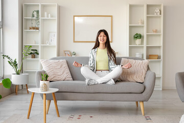 Young woman meditating on sofa at home