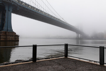 Waterfront view of the Manhattan Bridge covered by dense fog