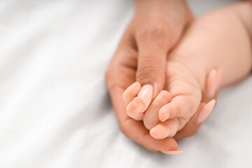 Mother's hand holding tiny baby arm on bed at home, closeup