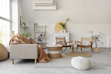 Interior of stylish living room with cozy grey sofa, coffee table, pouf and houseplants