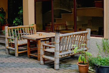 Rustic bamboo table and benches set up in outdoor café, surrounded by potted plants. Sustainable furniture emphasizes eco-friendly living and traditional craftsmanship