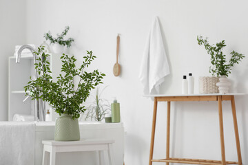 Vases with green blossoming branches on stepladder near bathtub in stylish bathroom
