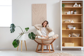 Young woman with headphones listening to music in cocoon chair at home
