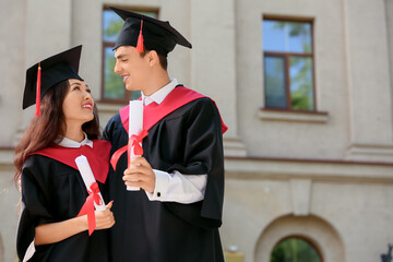 Couple of happy graduating students with diplomas hugging near university