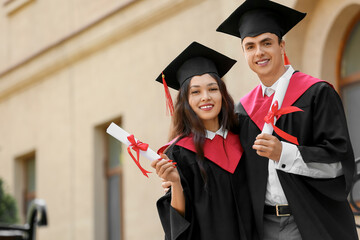 Couple of happy graduating students with diplomas hugging near university