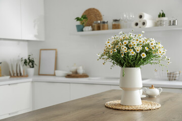 Vase with chamomiles on table in kitchen