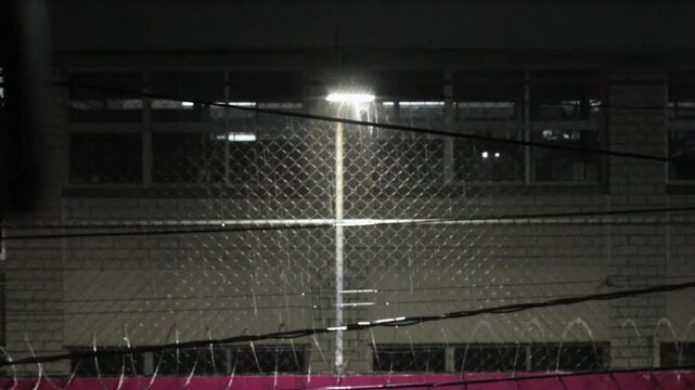 Farol frente reja met&aacute;lica iluminando las gotas de lluvia que est&aacute;n cayendo cerca de este. 