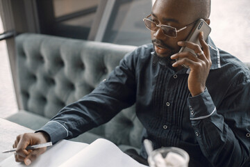 Black man sitting in a cafe with a cup of latte and using a phone
