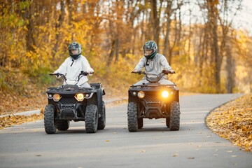 Fototapeta premium Man and woman driving quad bikes in autumn forest