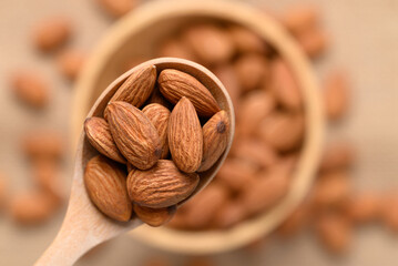 Raw almond nut seed in wooden spoon and bowl, Top view