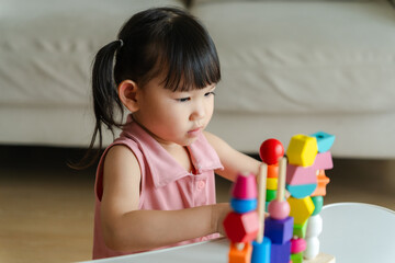 3 year old girl having fun playing with colorful geometric shape wooden blocks educational toys at...
