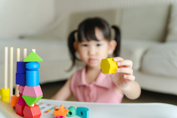 3 year old girl having fun playing with colorful geometric shape wooden blocks educational toys at...