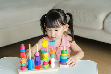 3 year old girl having fun playing with colorful geometric shape wooden blocks educational toys at...