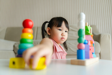 3 year old girl having fun playing with colorful geometric shape wooden blocks educational toys at...
