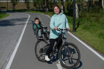 Caucasian woman riding a bicycle with her toddler son sitting behind her in a child seat. 