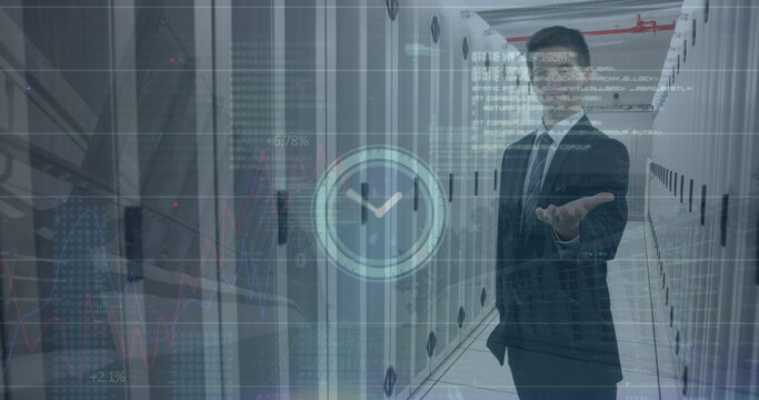 Image of clock icon over caucasian businessman holding an invisible object at server room
