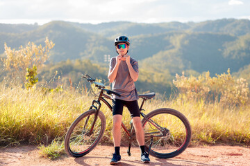Obraz premium Young male cyclist putting on his helmet while resting on a trail with mountain bike. Outdoor adventure, healthy lifestyle, and safety awareness in nature.