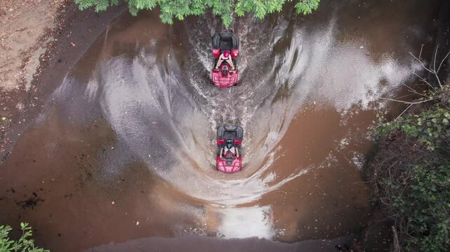 Overhead shot of six ATVs creating water splashes while crossing a muddy puddle in the forest in Costa Rica.
