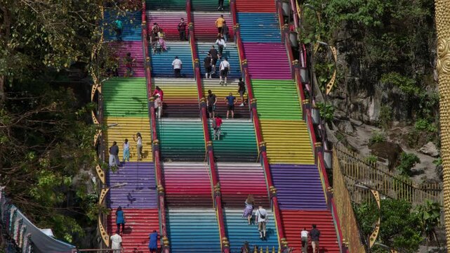 Visitors ascend and descend the vibrant, multicolored steps of the Batu Caves, a notable cultural and religious site