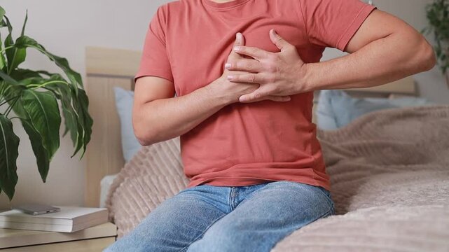 Close-up Man experiencing sharp pain in chest, holding hands on sore spot. Heart attack or infarction. Cardiovascular diseases