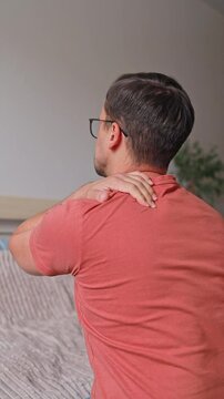 Vertical video from the back of a man suffering from pain and massaging his neck and shoulders at home, osteochondrosis, hernias and protrusions.