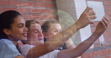 Image of financial graph and globe over happy diverse pupils taking selfie at school