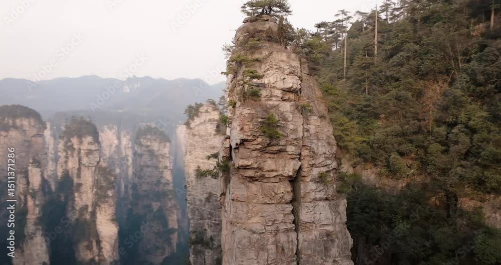 Poster close aerial view of a towering sandstone pinnacle with sparse trees growing on top, surrounded by c