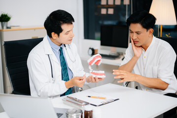 Obraz premium Asian dentist explains oral care using dental jaw model to male patient in clinic. Concept of dental hygiene, checkup, health education,
